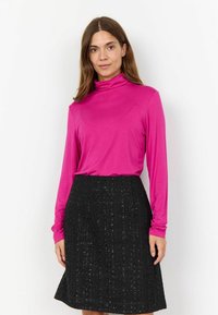 Haut à col roulé ajusté à manches longues en rose vif, associé à une jupe noire en A texturée présentant un motif de grille et un léger scintillement.