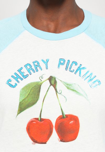 Close-up of a person wearing a white and light blue shirt with a cherry illustration and the text "CHERRY PICKING" above it.