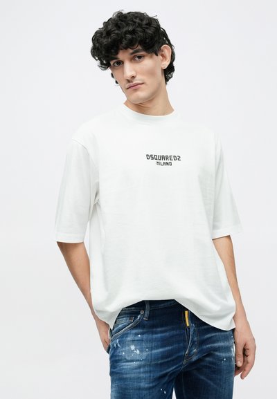 T-shirt bianca a maniche corte con logo nero "DSQUARED2 MILANO" al centro davanti, abbinata a jeans blu strappati.