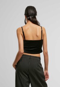 Černý sametový crop top s tenkými ramínky, spárovaný s proužkovanými kalhotami s vysokým pasem. Důraz na texturu a elegantní design.