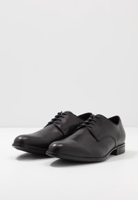 Chaussures habillées en cuir noir à finition lisse, bout arrondi et talon bas. Caractéristiques : fermeture à lacets et design minimaliste.