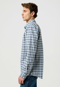 Camicia a maniche lunghe a quadri blu e bianchi, con colletto a bottone e taglio dritto. Dettaglio tasca sul lato sinistro del petto. Stile casual.