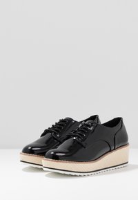 Chaussures plateforme en cuir verni noir avec une semelle intermédiaire tissée texturée et une semelle en caoutchouc blanche contrastante. Caractérisées par un bout rond et un design à lacets.