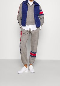 Conjunto de suéter gris con rayas rojas y azules, combinado con un chaleco acolchado azul. Las zapatillas blancas completan el atuendo, presentando un aspecto casual.