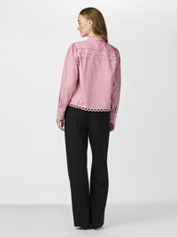Pink long-sleeve blouse with lace detailing on the shoulders and cuffs, paired with black wide-leg trousers. Smooth fabric.