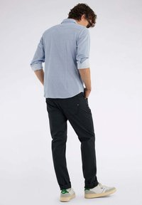 Camicia azzurro chiaro con un motivo testurizzato, abbinata a pantaloni scuri e sneakers color crema con accenti verdi. Maniche arrotolate visibili.