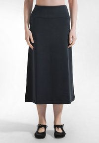 Persona con una falda midi negra de talle alto y zapatos planos negros con cordones, de pie frente a un fondo blanco liso.