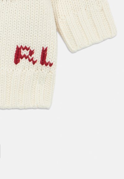 Vit stickad ärm med ribbad manschett och röda broderade bokstäver "FAL" nära handleden mot en enkel vit bakgrund.