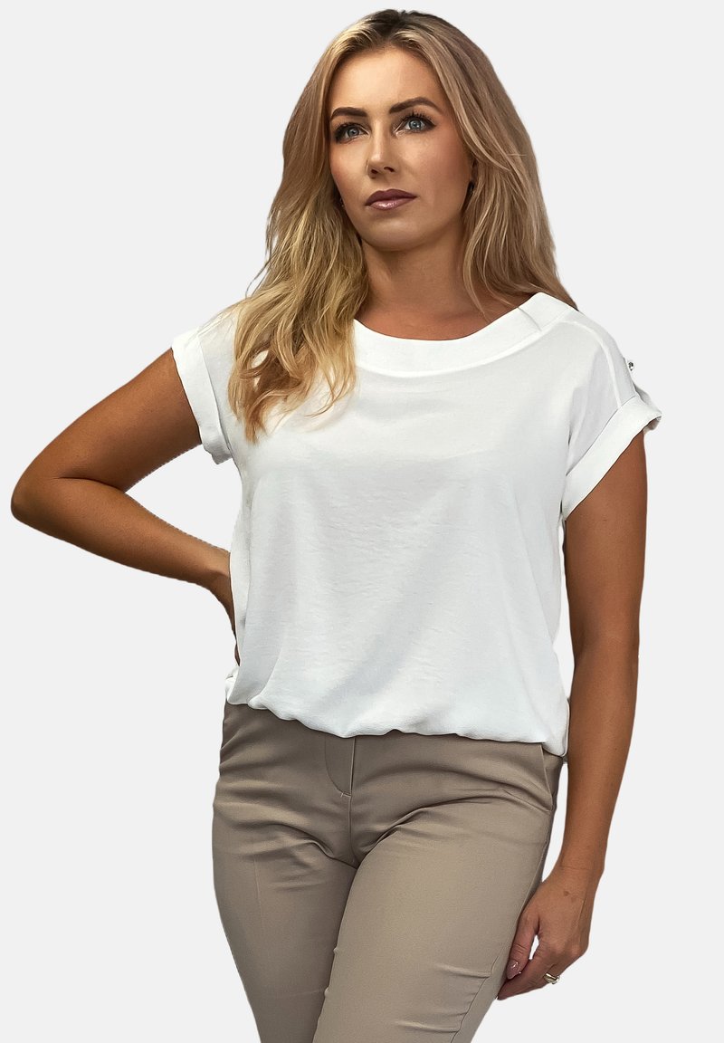 Biała bluzka na krótki rękaw z podwiniętymi mankietami, okrągłym dekoltem i miękką teksturą. Połączona z jasnobrązowymi dopasowanymi spodniami. Prosty fason.