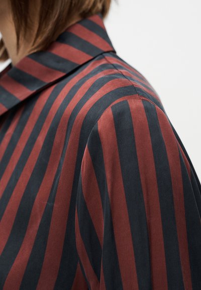 Bordó és tengerészkék csíkos ing hegyes gallérral, sima textúrával és laza szabással. A csíkok szélessége változó a szöveten.