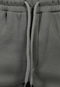 Graue Jogginghose aus strukturiertem Stoff, mit elastischem Bund und geflochtenen Kordeln. Zwei seitliche Taschen sichtbar.