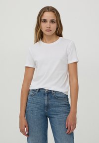 T-shirt bianca di cotone con maniche corte, scollo rotondo, indossata con jeans in denim blu a vita alta, lavaggio chiaro con taglio classico.