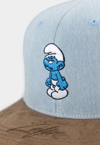 Hellblaues Cap mit einem blauen gestickten Schlumpf-Charakter auf der Vorderseite. Weiches Denim-Material mit einem braunen Wildleder-Schild und strukturierter Oberfläche.