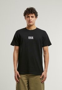 Svart bomull t-skjorte med hvit "USA" grafikk på brystet. Korte ermer og rund hals. Standard passform med en jevn tekstur.