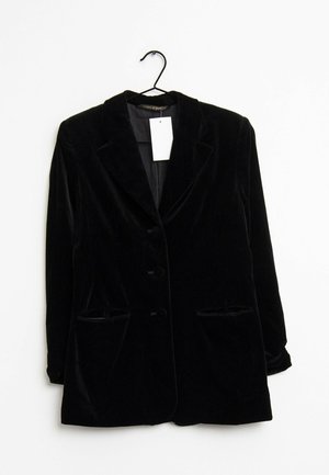 Černé sametové sako se třemi knoflíky a dvěma předními kapsami zavěšené na černém ramínku na bílém pozadí.