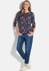 Marinebluse mit pinken und cremefarbenen Blattmustern, Rundhalsausschnitt und Dreiviertelärmeln, kombiniert mit blauen Jeans und weißen Sneakern.