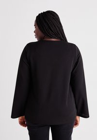 Black long-sleeve top with a rounded neckline and textured fabric. Features a straight cut and slight flare at the sleeves.