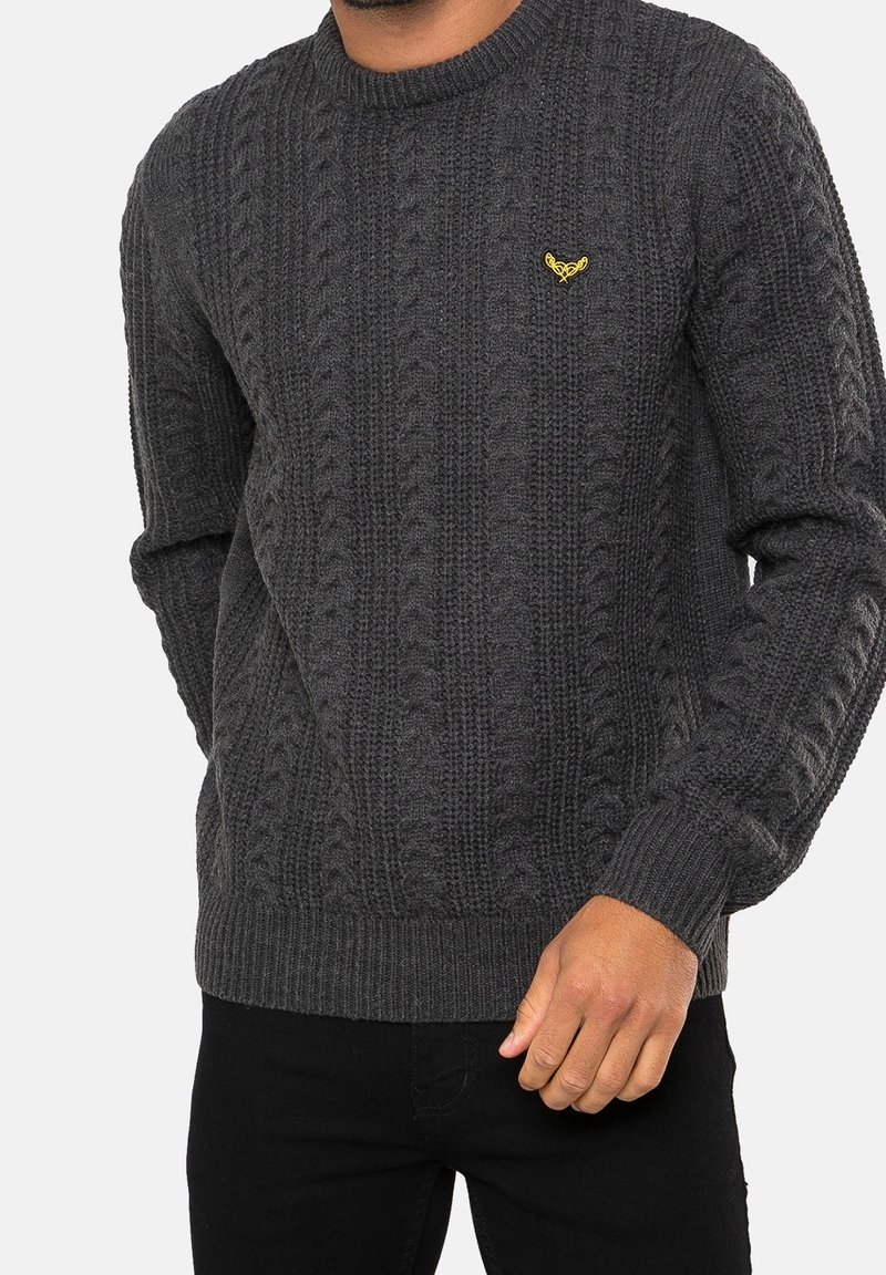 Mörkgrå stickad tröja med en texturerad kabeldesign. Har en rund halsringning och en liten gul logotyp på bröstet.