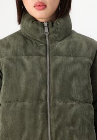 Groene corduroy pufferjack met een hoge kraag, ritssluiting en verticale ribbeltextuur. Heeft een standaard pasvorm en een geborduurde ontwerp.