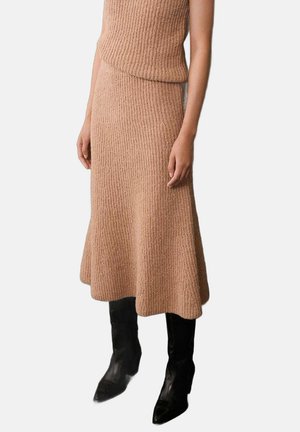 Dzianinowy dwuczęściowy zestaw w jasnym beżu z dopasowaną bluzką i rozszerzaną spódnicą midi, uzupełniony czarnymi kozakiem na wysokim obcasie sięgającymi do kolan.