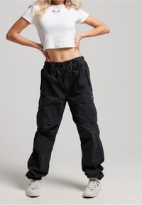 Czarne spodnie cargo w luźnym kroju, z regulowanym pasem, bocznymi kieszeniami i mankietami. Połączone z białą, krótką koszulką.