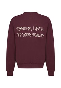 Bordeaux sweatshirt met een ronde hals, geribbelde boorden en onafgebroken randafwerking. Op de achterkant staat de tekst "DREAM UNTIL IT'S YOUR REALITY" in het wit.