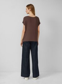 Bruine top met korte mouwen, gecombineerd met donkerdenim broek met wijde pijpen en witte sneakers. Gladde stof met een relaxte pasvorm en ronde halslijn.