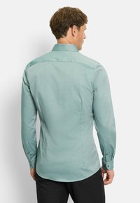 Knopfhemd in hellem Teal mit dezentem Muster, langen Ärmeln, klassischem Kragen und abgerundetem Saum. Verfügt über Manschettenknöpfe und eine taillierte Passform.