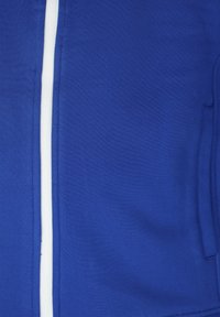 Blaues Sportjackett aus glattem Stoff, mit einem weißen Reißverschluss und Nähten, sowie seitlichen Taschen, die ins Design integriert sind.