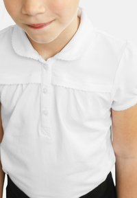 Polo à manches courtes blanc avec un col rond et une bordure festonnée, comprenant un patte de boutonnage avec trois boutons et un détail froncé sous l'épaule.