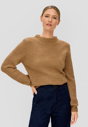 Bruine rib gebreide trui met een hoge hals en lange mouwen, gecombineerd met donkere denim jeans. De textuur is grof en warm.