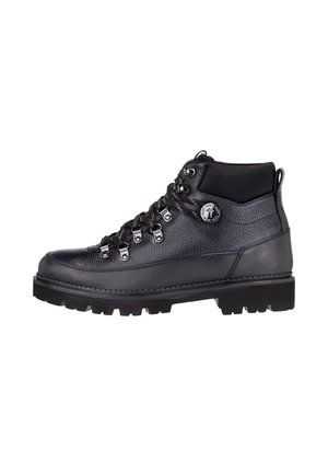 Schwarzer Leder-Wanderschuh mit Metallösen, dicker Profilsohle, gepolstertem Schaft und rundem Logo-Abzeichen am Knöchel.