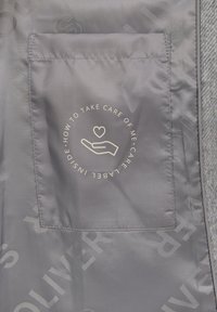 Tissu gris avec une poche affichant un design d'étiquette de soin, du texte entourant une icône de main et un cœur. Le texte est circulaire, avec des couleurs claires contrastantes.