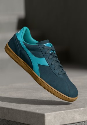 Blue and teal athletic shoes feature a suede and mesh upper, with a rubber gum sole and a lace-up design. Notable side accents in teal.
