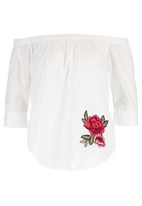 Blouse blanche à épaules dégagées avec manches trois-quarts et broderie florale rouge sur le côté inférieur droit.