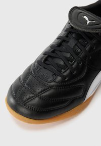 Black leather Puma sneaker with gum sole, black laces, stitched detailing, and Puma logo on tongue against white background.