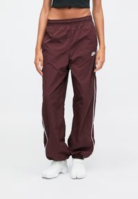 Burgundské vetrovky s bielymi postrannými pruhmi, elastickým pásom a malým logom na ľavom stehne. Materiál je hladký a ľahký.