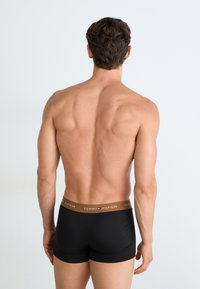 Boxers en coton noirs avec une taille brown ornée du logo "TOMMY HILFIGER", vus de dos, avec la peau visible au-dessus.