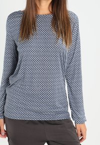 Pitkähihaine t-paita tummansinisenä, jossa on valkoinen geometrinen kuvio. Pehmeä, joustava kangas, jossa on rento malli ja pyöreä kaula-aukko.