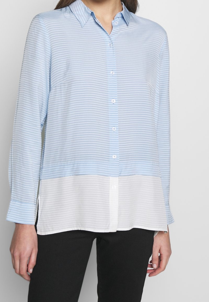 Camicia a righe blu chiaro e bianca con maniche lunghe, apertura frontale con bottoni, colletto e orlo inferiore bianco, realizzata in un tessuto morbido e leggero.