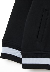 Felpa nera con polsini a coste decorati con strisce azzurre e bianche, texture spazzolata e dettaglio di tasca laterale.