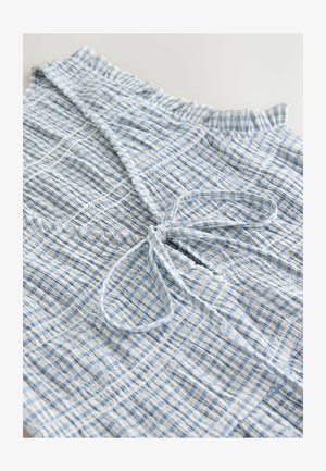 Világoskék-fehér kockás felső, megkötővel, ráncolt textúrával és fodros nyakkivágással. Könnyű, szőtt anyagból készült.