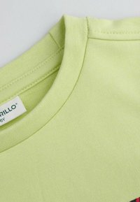 Jasnozielona bawełniana koszulka z okrągłym dekoltem, charakteryzująca się gładką fakturą i widoczną metką w okolicy kołnierza. Brak grafik.