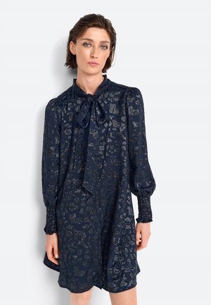 Abito blu navy con un motivo leopardato testurizzato, maniche lunghe e scollatura con fiocco. Presenta polsini arricciati e una vestibilità rilassata.