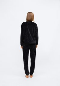 Zwart velours lounge-outfit bestaande uit een relaxte lange mouw top en taps toelopende broek, beide met een zachte textuur en elastische boorden.