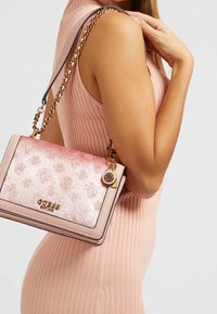 Borsa Guess rosa con un design floreale texture, hardware dorato, tracolla a catena e un charm. Forma rettangolare compatta con una finitura liscia.