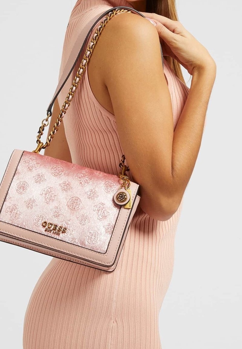 Borsa Guess rosa con un design floreale texture, hardware dorato, tracolla a catena e un charm. Forma rettangolare compatta con una finitura liscia.