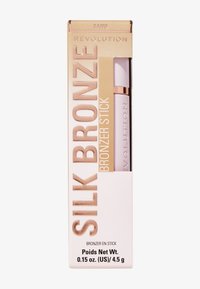 Bronzer-stav i en elegant, rosa innpakning inne i en gull- og kremfarget eske. Teksten inkluderer "Silk Bronze" og "Bronzer Stick," med fargen "Sand."