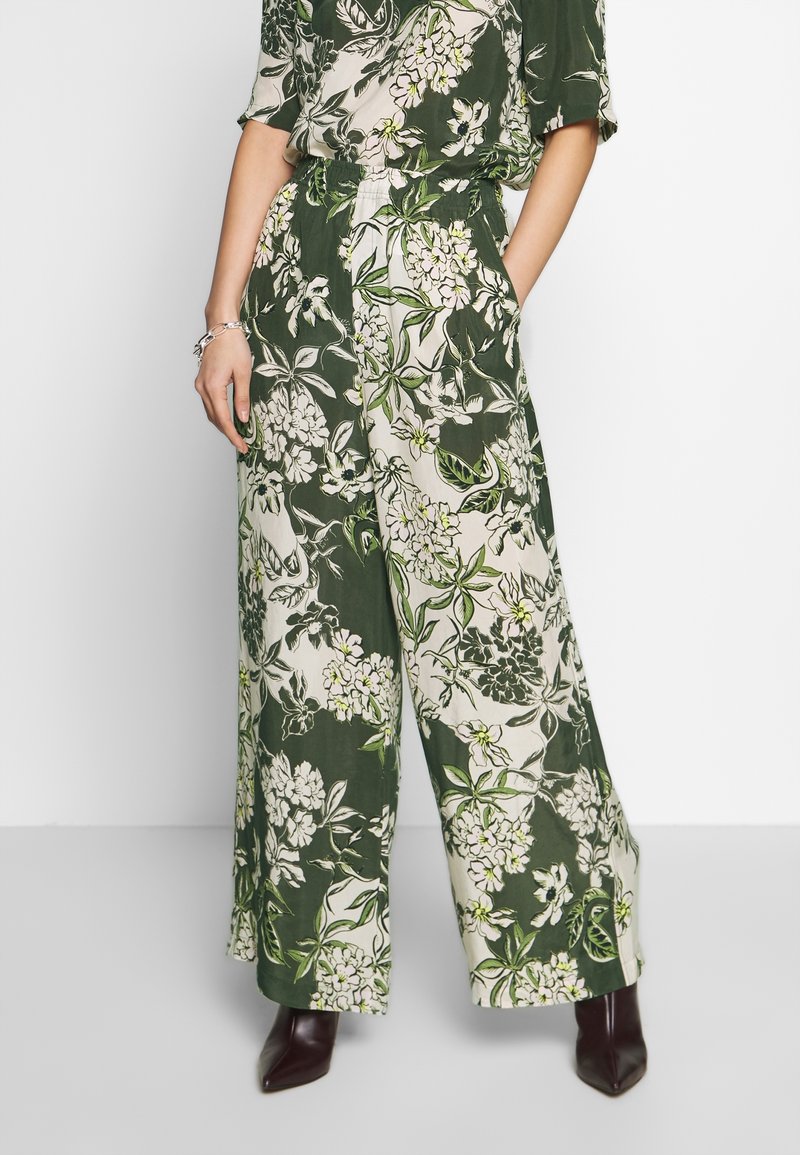 Pantalon ample vert et blanc avec taille élastique et imprimé floral, associé à des bottines pointues marron foncé.