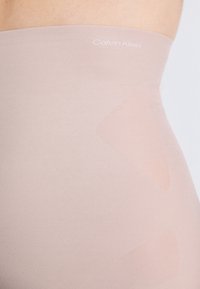 Korkeavyötäröinen alushousu, joka on nude-värinen ja sileäpintainen. Yläosassa on Calvin Kleinin logo ja se on suunniteltu saumattomaksi käytettäväksi.